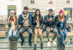 50576293 - multicultural group of friends using cellphones sitting in a row