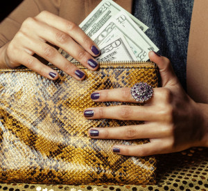 pretty fingers of african american woman holding money close up with purse, luxury jewellery on python clutch, cash for gifts